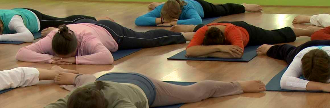 Multiple Dru yoga participants lying face down with head in hands and legs spread - the crocodile pose